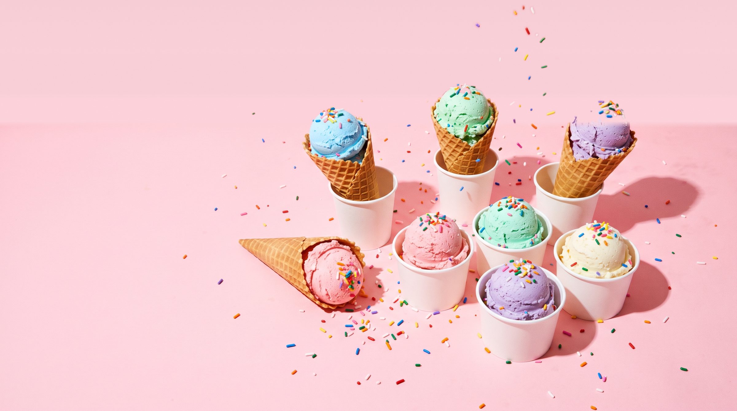 Scoops of pastel ice cream in cones and cups with sprinkles on a pink background